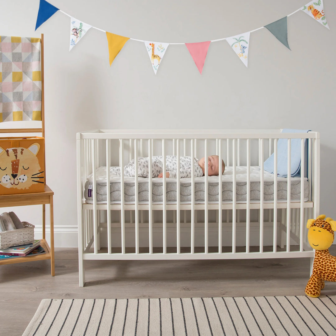 ClevaMama Premium Deluxe ClevaFoam Pocket Sprung Mattress in white baby cot — baby sleeping peacefully on breathable ClevaFoam and pocket sprung mattress designed for comfort, support, and airflow; shown in modern nursery with neutral decor and soft furnishings.