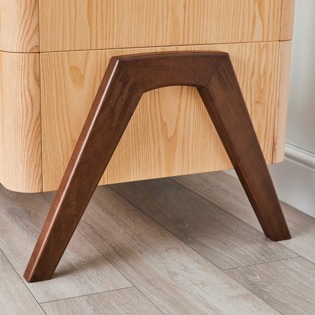close up lifestyle image of the legs of the Hera Cot Bed in Natural Ash and Walnut
