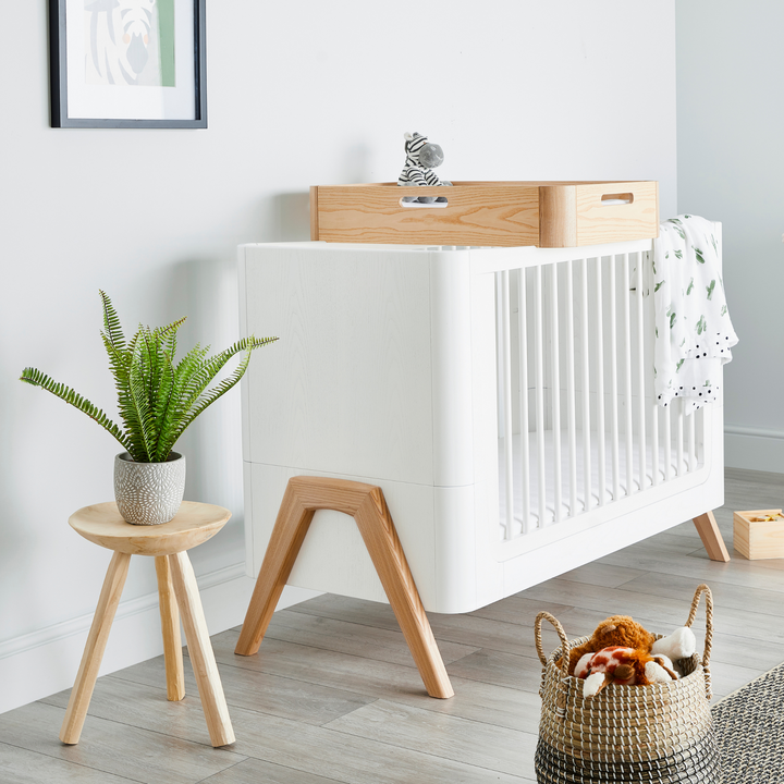 Gaia Baby Lifestyle image of the Hera Cot Bed in Scandi White and Natural with the low cot bed mattress setting with the Hera Cot Top Changing Station