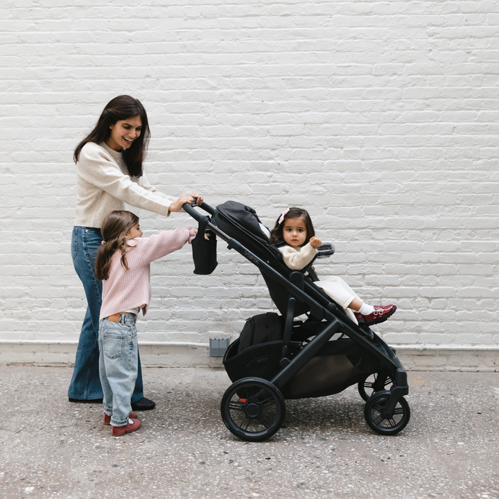 Smiling mother with two children using UPPAbaby Vista V2 stroller in black, versatile pushchair with large wheels and storage basket, perfect for toddlers and growing families