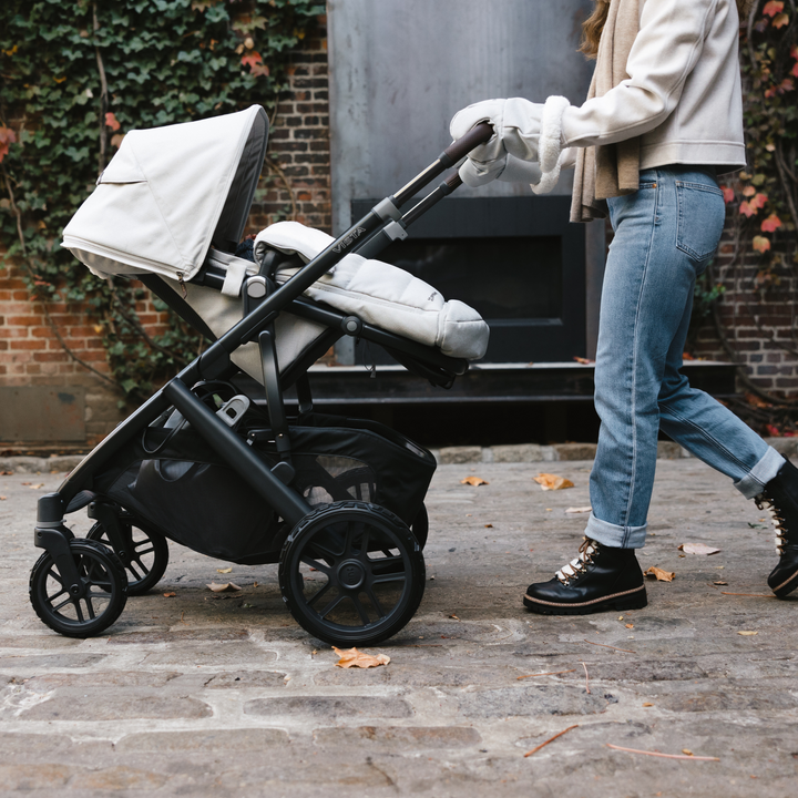 Parent pushing the UPPAbaby VISTA V2 stroller in Declan Oatmeal, side view with toddler seat fully reclined for comfort, featuring extended canopy, padded footmuff, large storage basket, and durable all-terrain wheels – stylish and practical pushchair for urban and outdoor strolls.