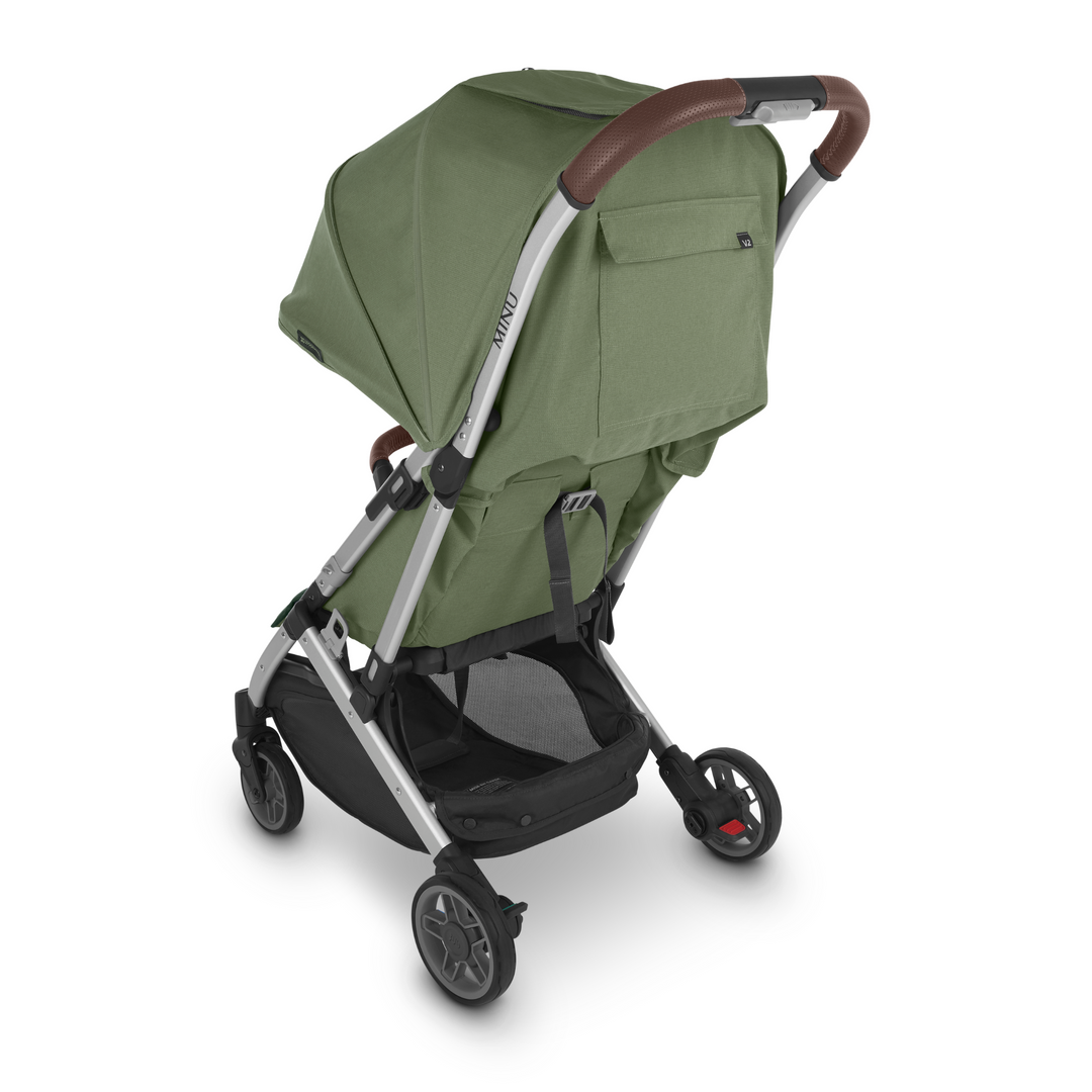 UPPAbaby Minu V2 lightweight travel stroller in Emelia which is a green fabric with chestnut REACH certified leather accents on a silver frame. The stroller is facing the back of the image, so this shot showcases the handy pocket on the back of the stroller and the easy recline mechanism. The 9kg basket is also visible