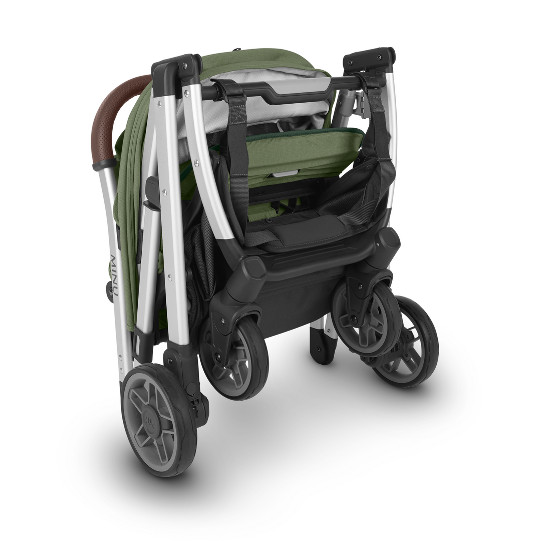 UPPAbaby Minu V2 lightweight travel stroller in Emelia which is a green fabric with chestnut REACH certified leather accents on a silver frame.  This image is the stroller folded to showcase the small footprint. While folded, the Minu V2 is airline friendly.