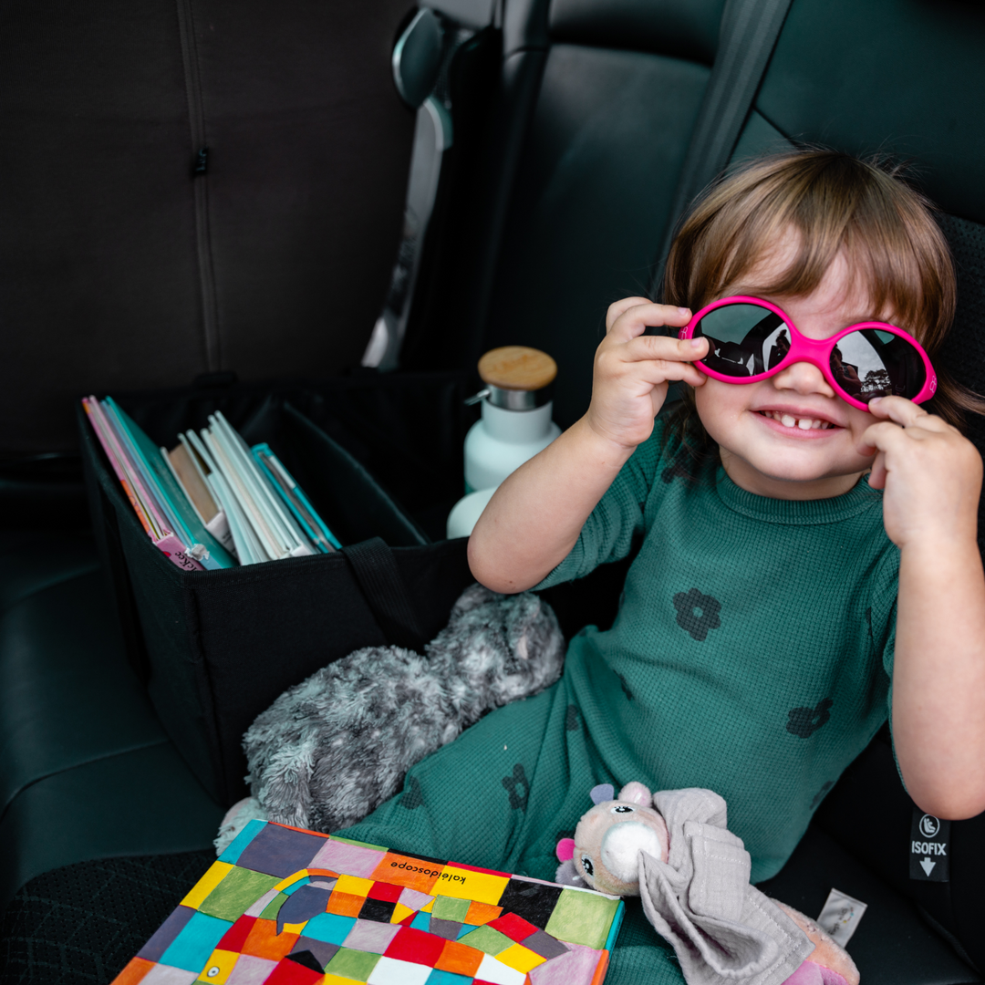 Ezimoov Car Organiser Caddy on back seat of car holding books with cute child wearing pink sunglasses.