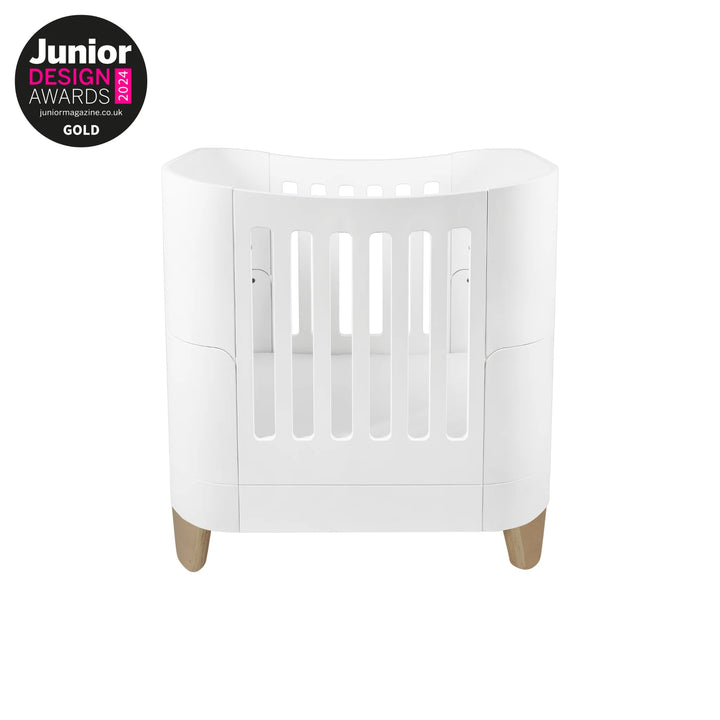 Serena Mini Cot with natural wooden legs in a modern white curved design, award-winning Gold at the Junior Design Awards, premium space-saving baby cot for newborns and small nursery spaces.