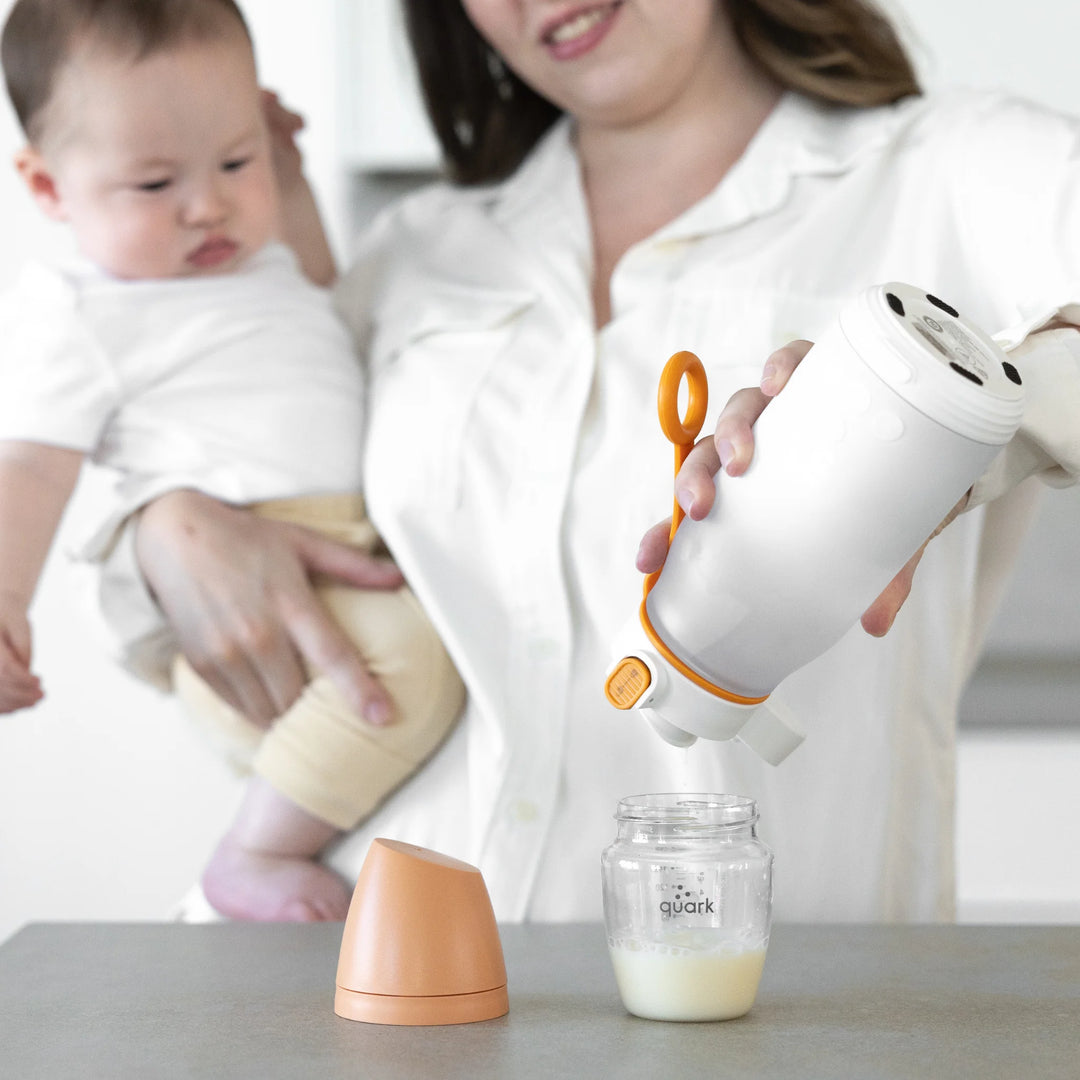 Parent using Buubi by Quark smart portable baby bottle warmer to heat milk in a Quark baby bottle while holding infant, convenient rechargeable milk warmer for on-the-go feeding