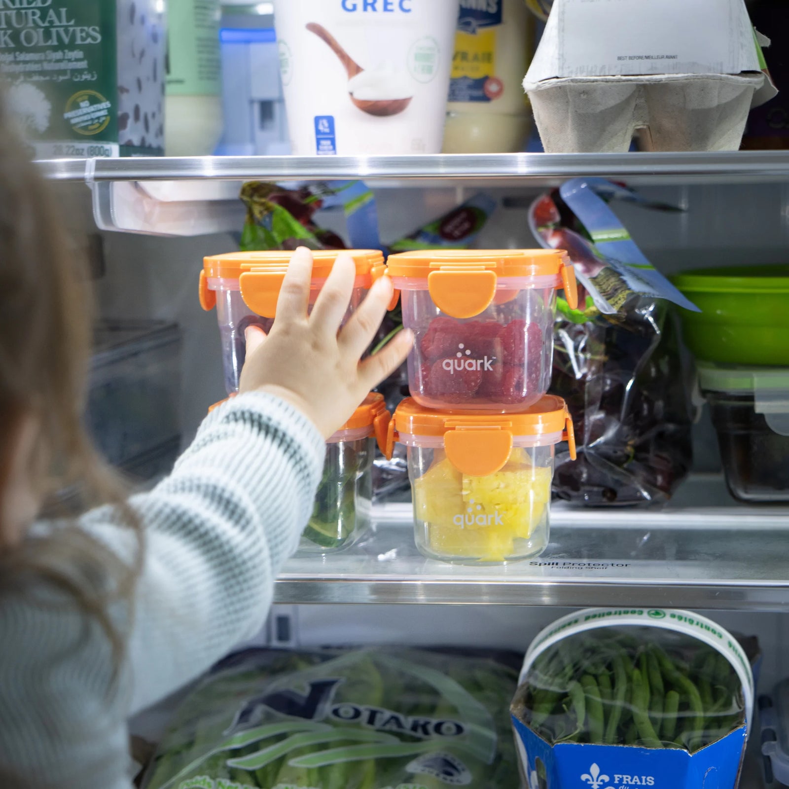 Child reaching for Storri food storage containers by Quark Baby in the fridge — airtight, BPA-free glass jars with silicone lids for baby food and snacks.