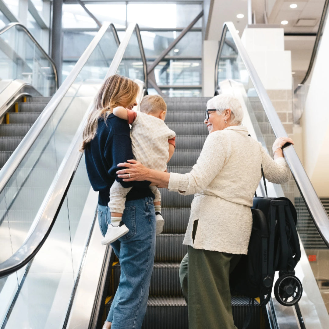“Family travelling with folded UPPAbaby MINU V3 stroller on escalator in airport or shopping centre