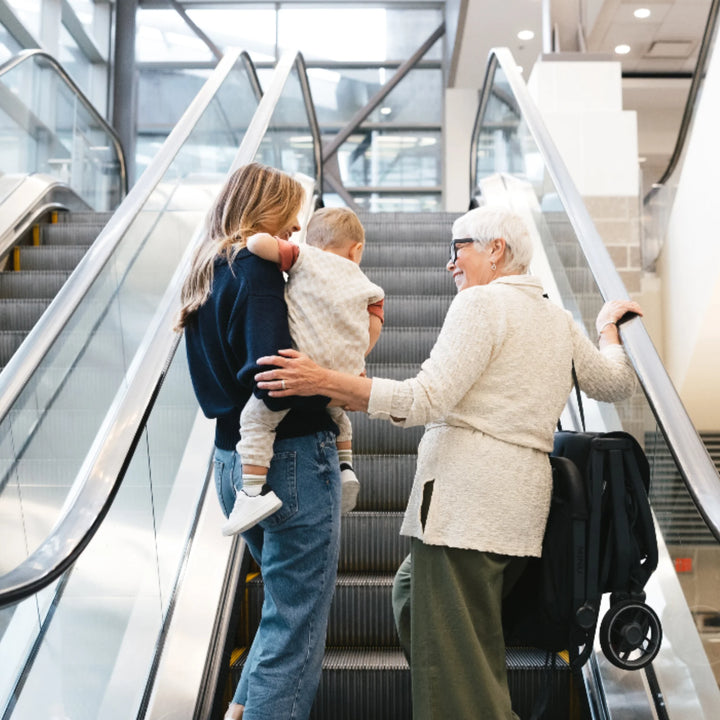 “Family travelling with folded UPPAbaby MINU V3 stroller on escalator in airport or shopping centre