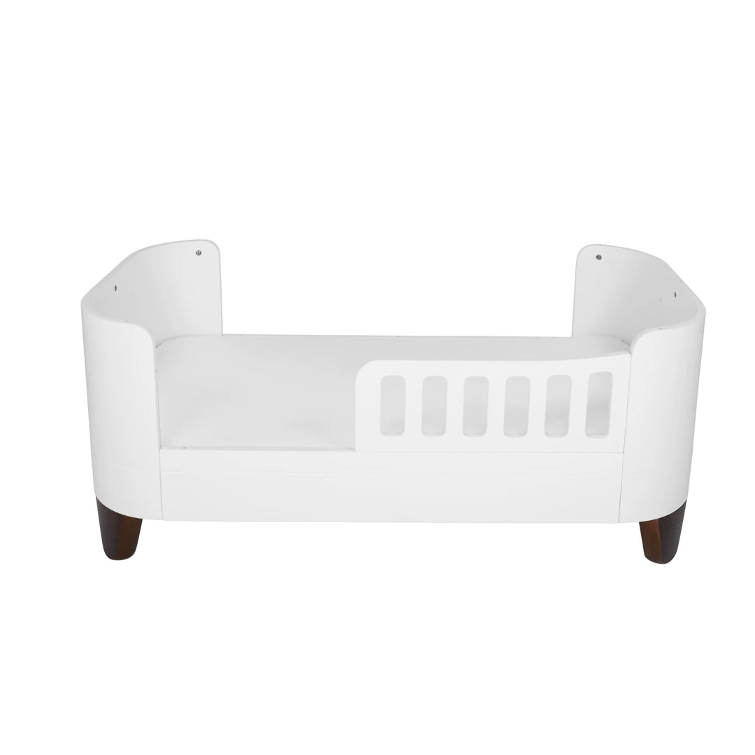 Gaia Baby Serena First Bed with toddler rail and walnut legs, shown in its low transitional setup, featuring the brand’s signature curved design for safe, stylish toddler sleep as part of the Serena nursery furniture system.
