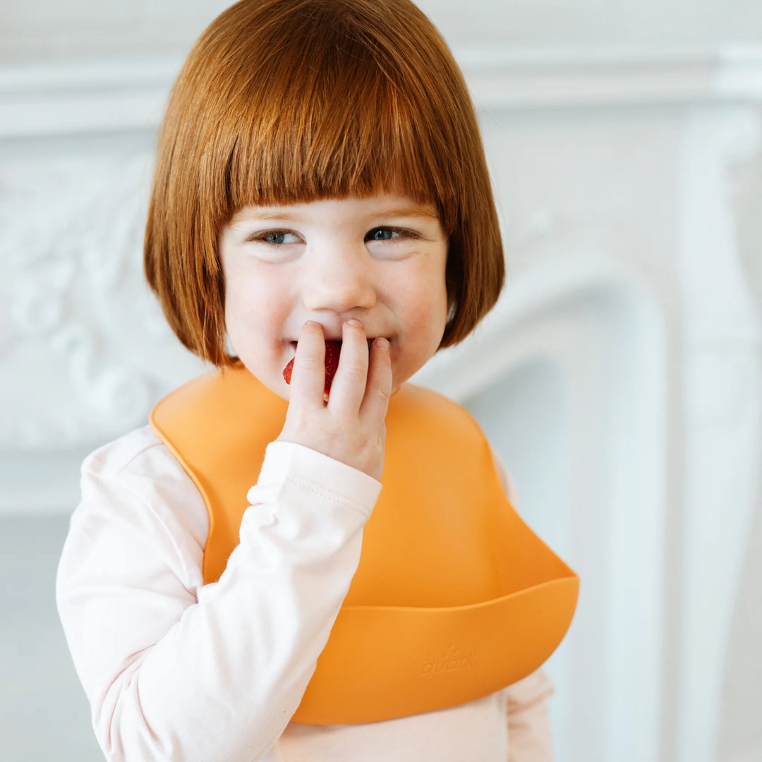 Feedi by Quark silicone baby feeding set in use, toddler eating fresh fruit from BPA-free suction plate with matching bib, promoting self-feeding and baby-led weaning.