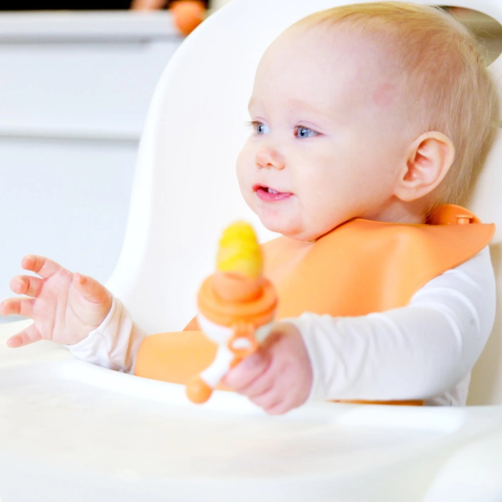 Baby sitting in high chair using Fruuti by Quark silicone fruit feeder – BPA-free teething feeder for introducing solids and encouraging safe self-feeding.