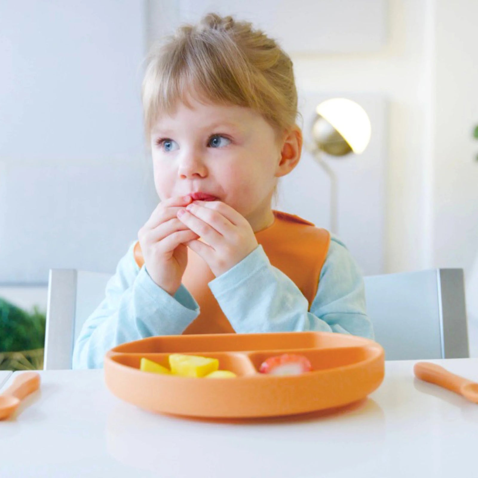 Toddler eating fruit using Feedi by Quark silicone baby feeding set, BPA-free suction plate, spoon, and bib promoting self-feeding and baby-led weaning at mealtime.