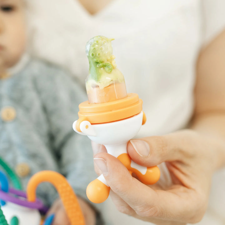 Parent holding a Fruuti by Quark silicone baby feeder filled with fresh fruit purée for safe baby-led weaning, reusable BPA-free baby feeding tool promoting self-feeding and teething relief.