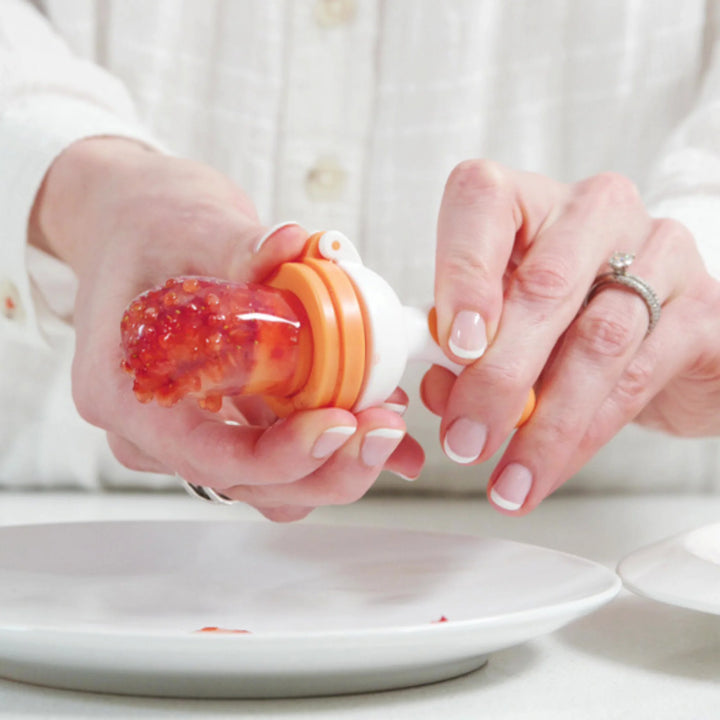Close-up of hands preparing a Fruuti by Quark silicone baby feeder with fresh strawberry purée, BPA-free reusable baby weaning feeder for introducing solid foods and encouraging safe self-feeding.