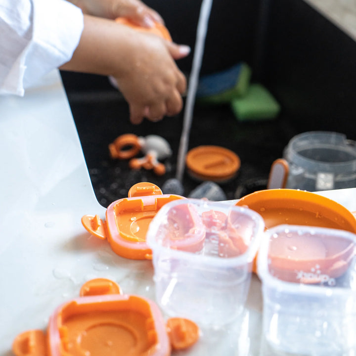 Washing Storri food storage containers by Quark Baby at the sink — BPA-free, dishwasher-safe glass jars with silicone lids for safe, reusable baby food storage.