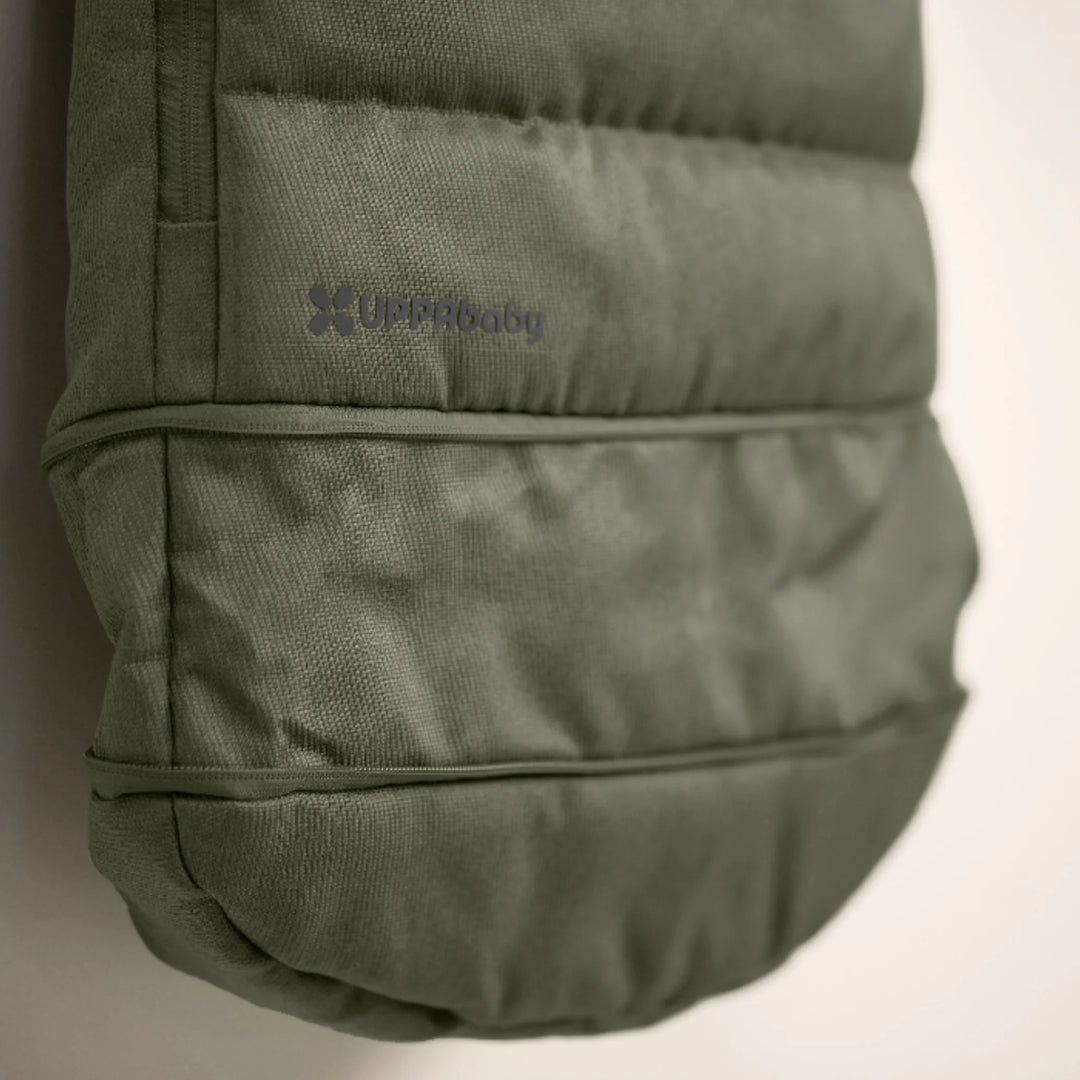 Close-up of UPPAbaby 2-in-1 Seasonal Cozy Ganoosh stroller footmuff in green, showing quilted windproof fabric, premium stitching, and subtle UPPAbaby logo for durable cold-weather protection.