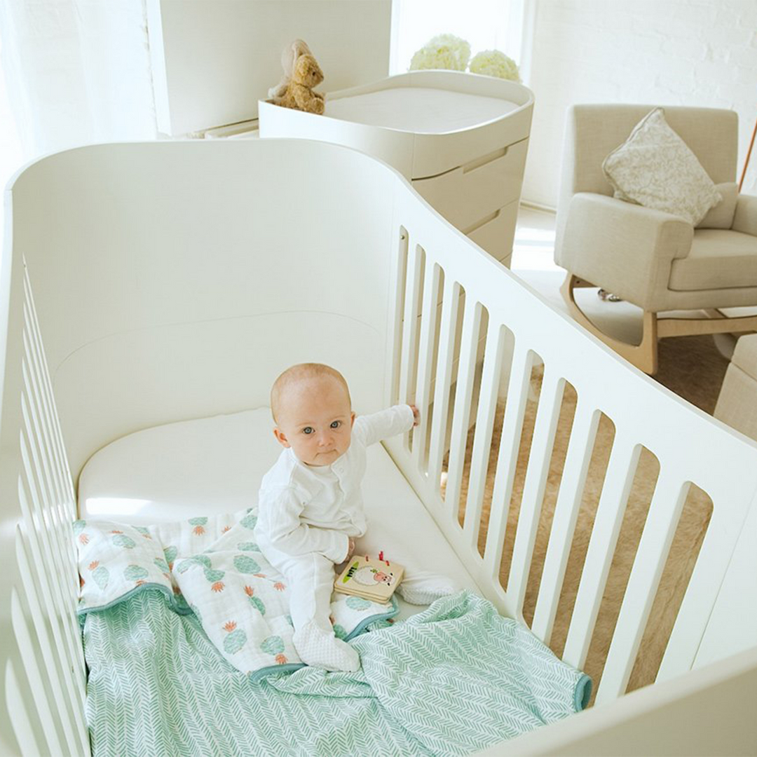 Serena Cot Bed All White low mattress  lifestyle image of baby sitting in the cot