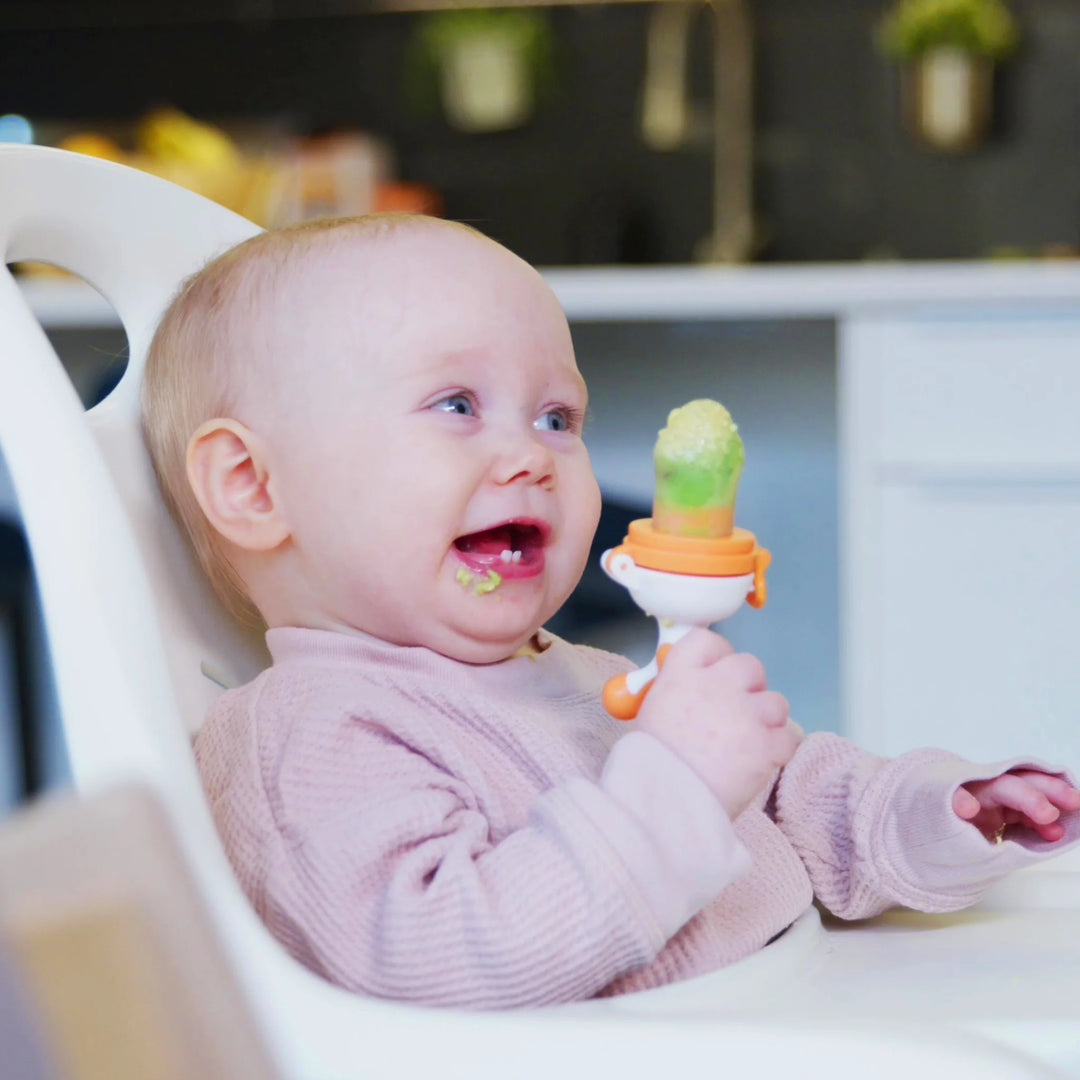 Close-up of hands preparing a Fruuti by Quark silicone baby feeder with fresh strawberry purée, BPA-free reusable baby weaning feeder for introducing solid foods and encouraging safe self-feeding.