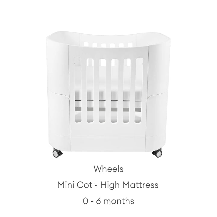 Serena Mini Cot in the high-mattress position for newborns aged 0–6 months, shown with optional wheels for easy mobility, featuring a modern white curved design and breathable slatted sides.