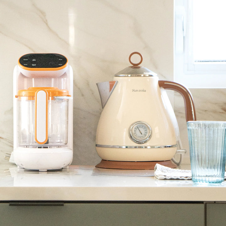 Quook by Quark 5-in-1 baby food maker on kitchen counter beside retro cream kettle — modern multifunctional baby food processor for blending, steaming, and warming homemade baby meals in stylish white and orange design