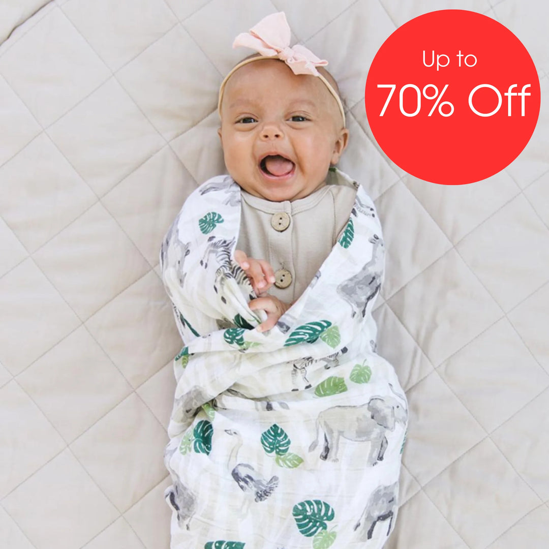 Smiling newborn baby wrapped in Bebe Au Lait muslin swaddle blanket with High Seas Moby jungle-animal print, soft breathable cotton swaddle shown on quilted mat with ‘Up to 70% Off’ sale badge.