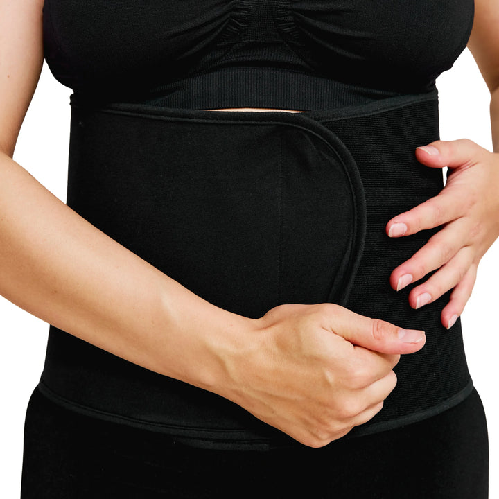 Person wearing a black post-birth compression binder on their abdomen against a white background
