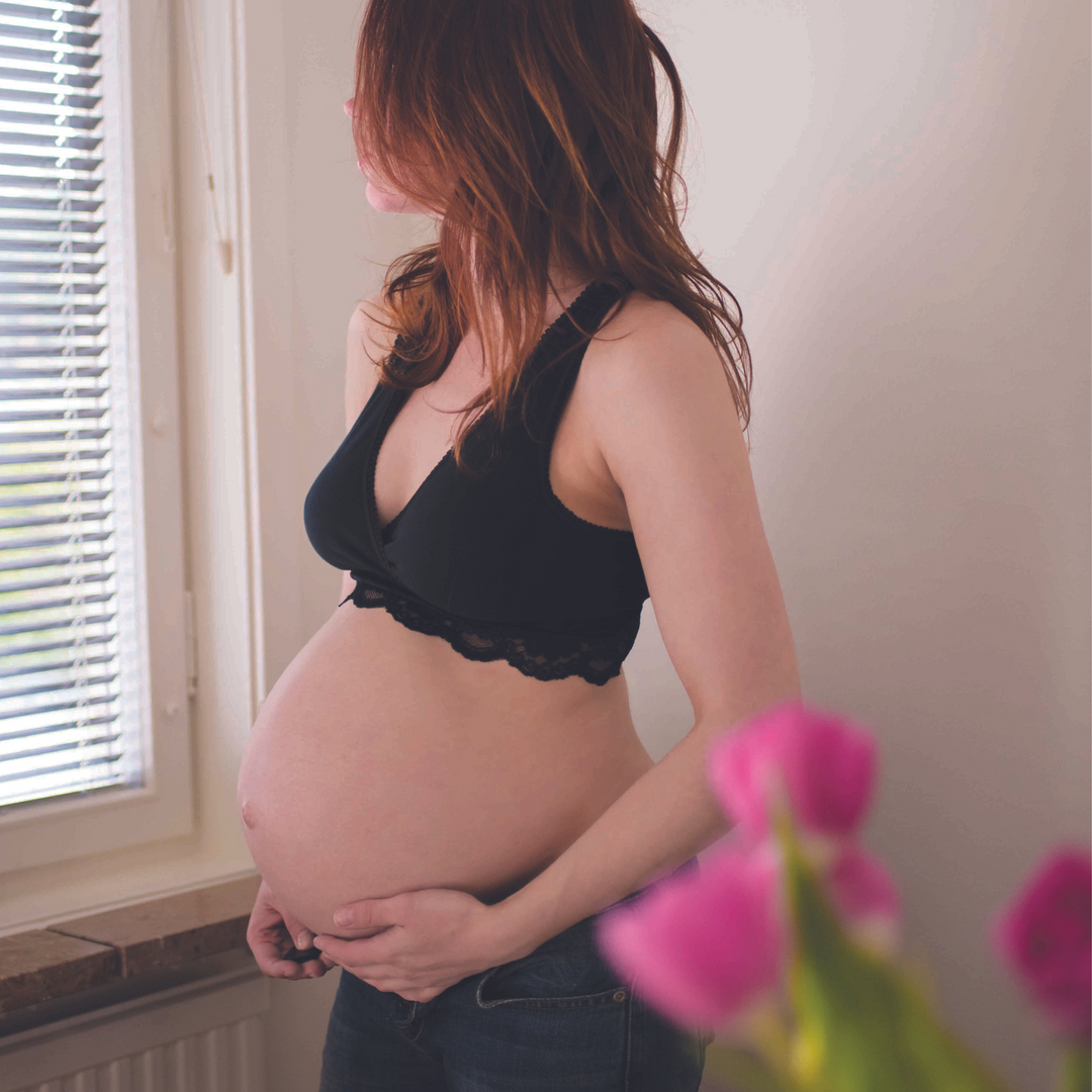 This image shows a pregnant mum wearing the Carriwell crossover maternity and nursing bra and looking out the window.