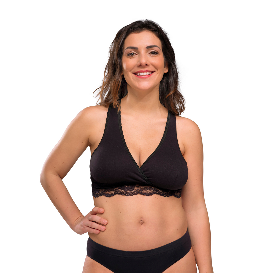 This image shows the black crossover and nursing bra on a smiling model with their hand on their hip.