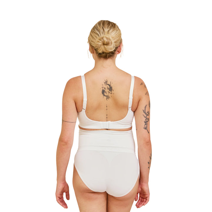 Back view of pregnant woman wearing white Carriwell maternity support band, showing smooth seamless fit and adjustable design for gentle lower back and abdominal support during pregnancy.