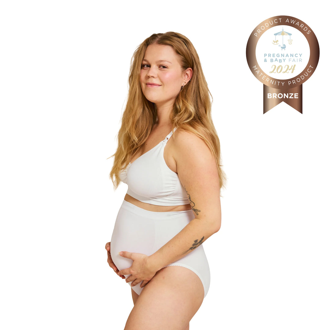 Side view of pregnant woman wearing white Carriwell maternity support panty, providing gentle belly and lower back support during pregnancy, with Pregnancy & Baby Fair award badge.