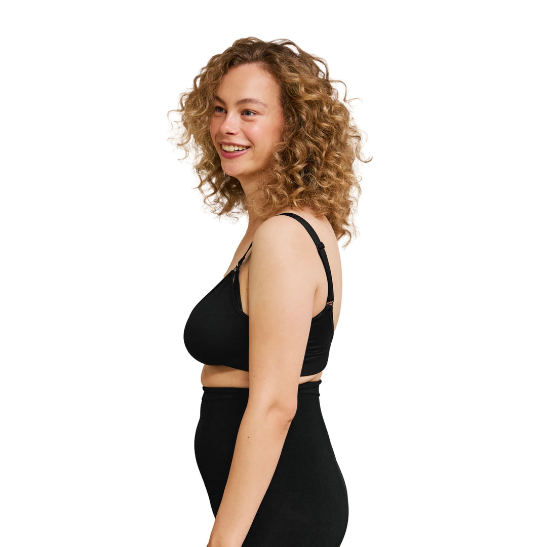 Woman wearing Carriwell feeding and maternity bra with support leggings from the side on a white background.