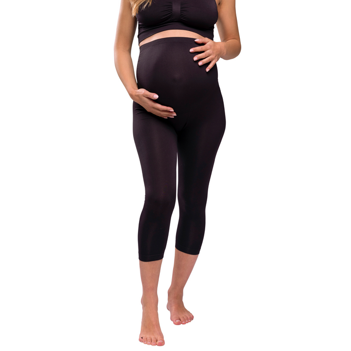 This image shows a model facing the camera wearing the leggings and holding her bump.