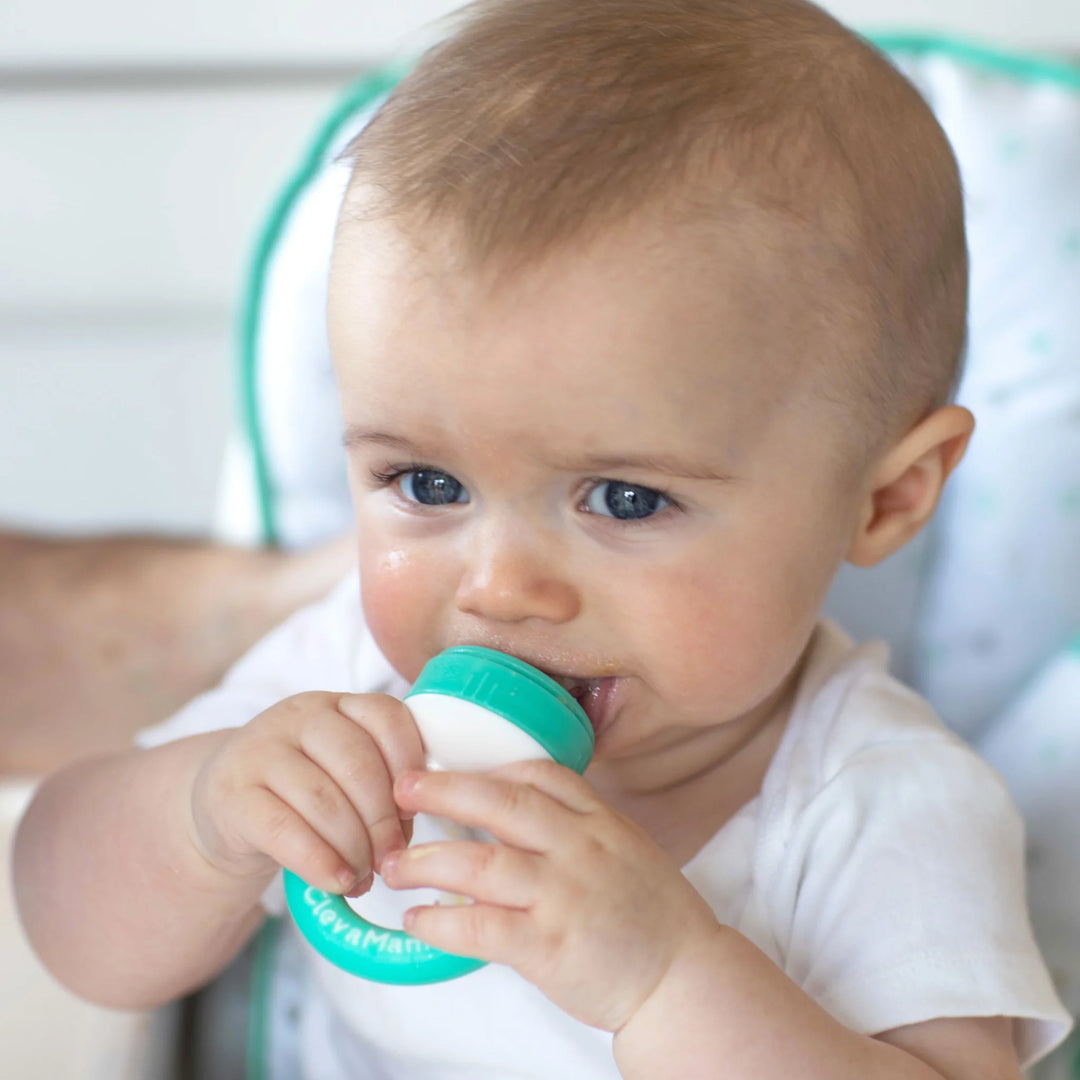 Baby using a ClevaMama ClevaFeed fruit feeder, holding the green ring handle and chewing the silicone tip.