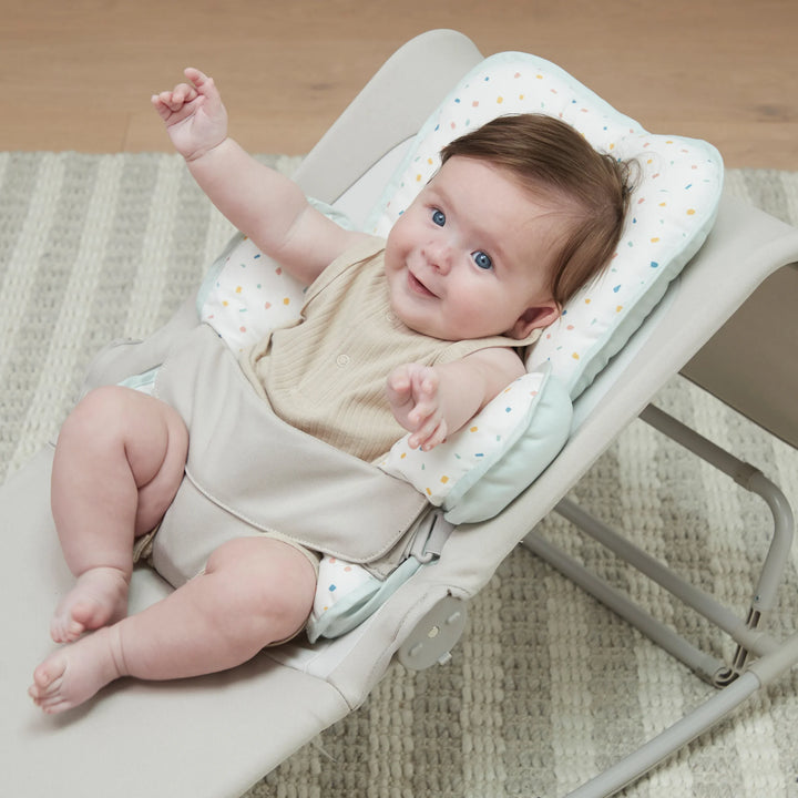 ClevaMama ClevaFoam Head and Neck Support Terrazzo design — happy baby reclining in bouncer with soft ClevaFoam head and body cushion. Ergonomic newborn insert designed for car seats, strollers, and bouncers to provide head and neck stability, prevent flat head syndrome, and ensure breathable comfort.