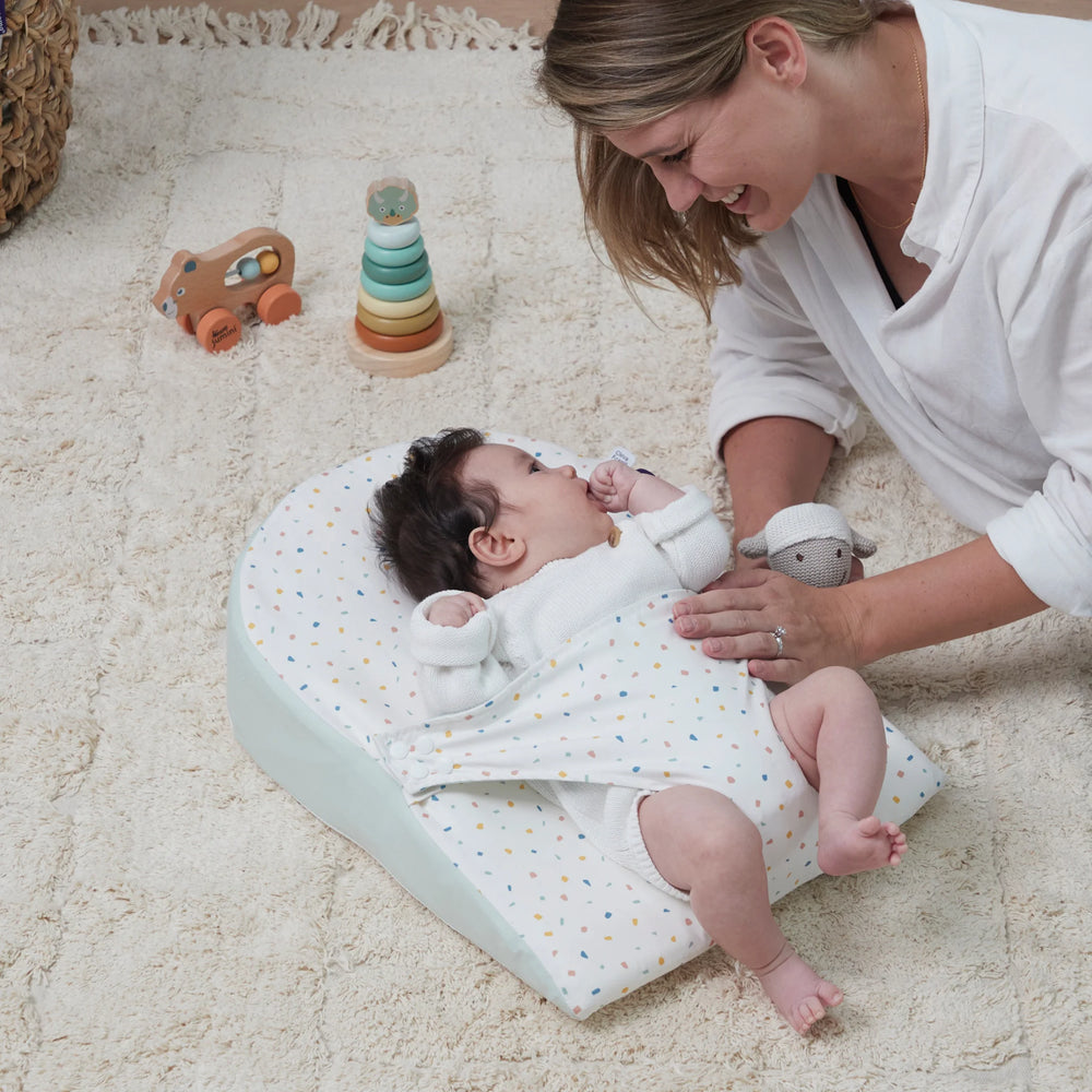 Baby lying on ClevaFoam reflux wedge on carpet with mum smiling at baby.