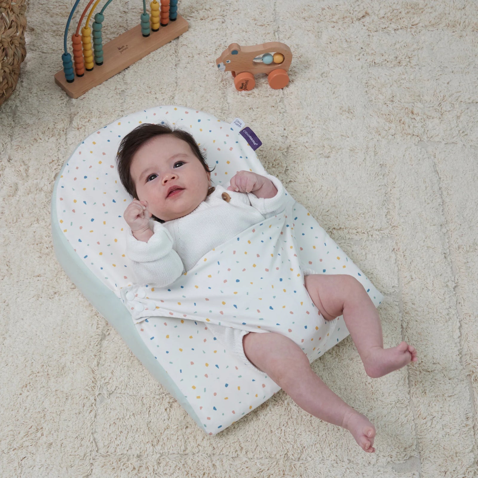 Baby resting on ClevaMama ClevaFoam Reflux Wedge Elevated Support in terrazzo design — breathable anti-reflux baby wedge with gentle incline to relieve reflux, colic, and congestion, promoting safe and comfortable sleep in a cosy nursery setting.