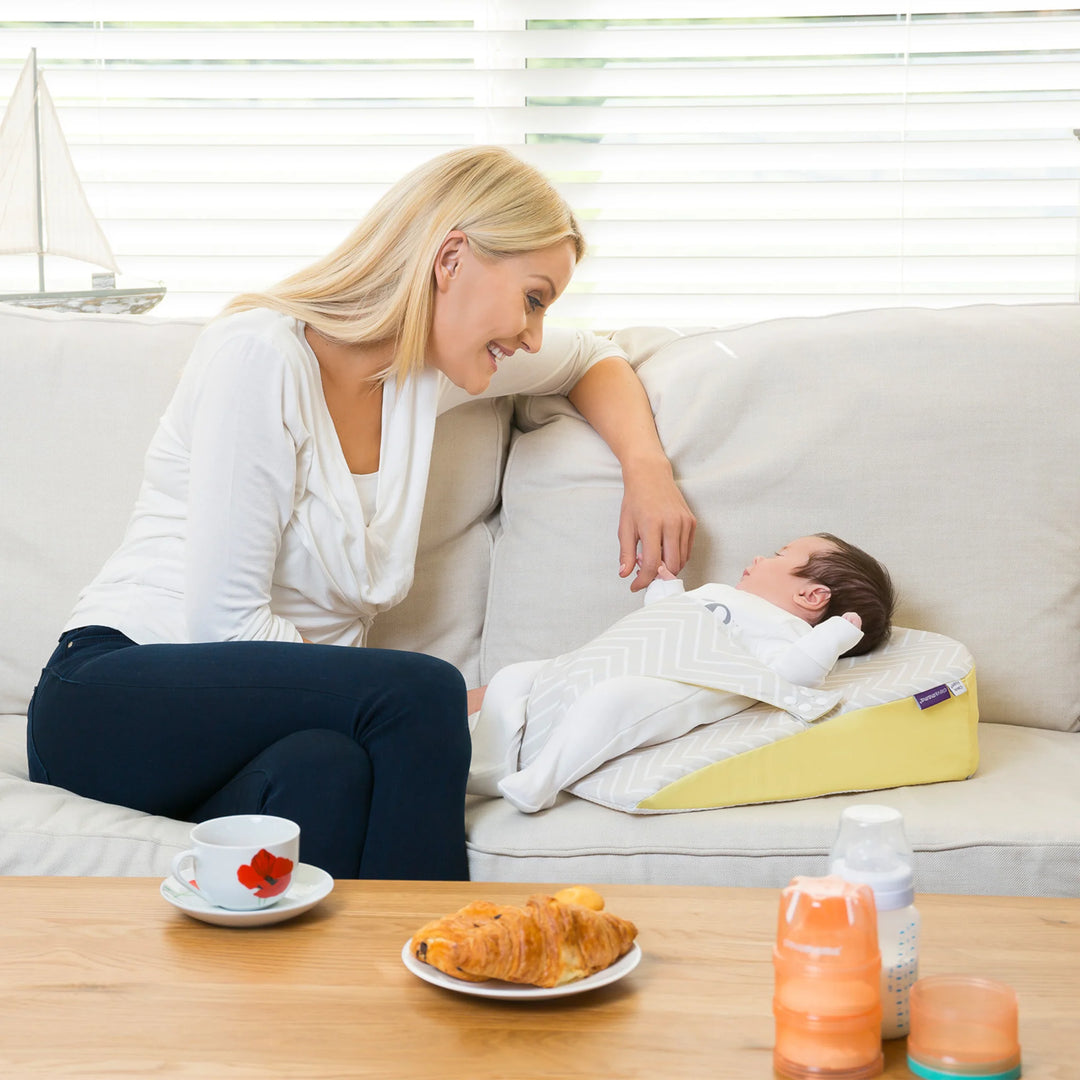 : Parent smiling at baby resting on ClevaMama ClevaFoam Reflux Wedge Elevated Support — breathable anti-reflux baby wedge that gently elevates infants to ease reflux, congestion, and colic, promoting safe and comfortable bonding time at home.