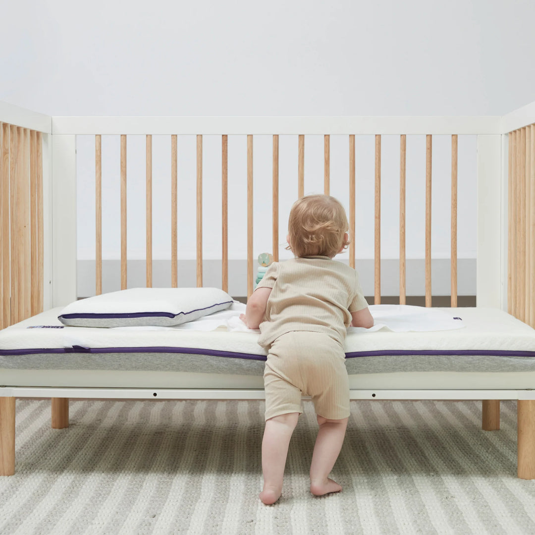 Toddler standing in cot with Clevamama ClevaFoam Waterproof Support Mattress – premium breathable baby mattress with waterproof protection, hypoallergenic reflex support foam, and removable washable cover for safe, hygienic, and comfortable sleep support.