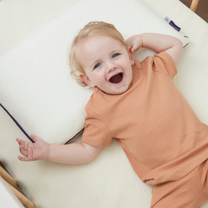 Happy toddler lying on Clevamama ClevaFoam® Toddler Pillow – breathable, hypoallergenic, and supportive memory foam pillow designed for children aged 12 months and older. Promotes healthy spine alignment and comfortable sleep while protecting against flat head syndrome. Perfect addition to toddler beds and nurseries.