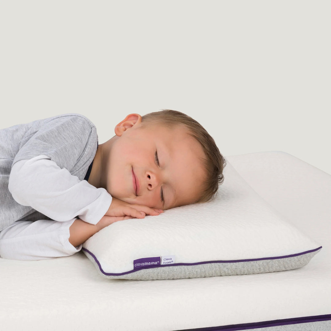 Sleeping toddler on Clevamama ClevaFoam® Toddler Pillow – breathable, hypoallergenic memory foam pillow for children aged 12 months and older. Provides ergonomic neck and head support for safe, restful sleep and helps promote healthy spine alignment in a cot or toddler bed.