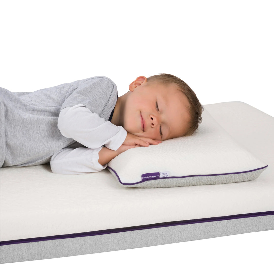 Toddler sleeping peacefully on Clevamama ClevaFoam® Toddler Pillow – breathable, hypoallergenic memory foam pillow for kids aged 12 months and older. Provides ergonomic head and neck support to promote healthy posture and comfortable, safe sleep in a cot or toddler bed.