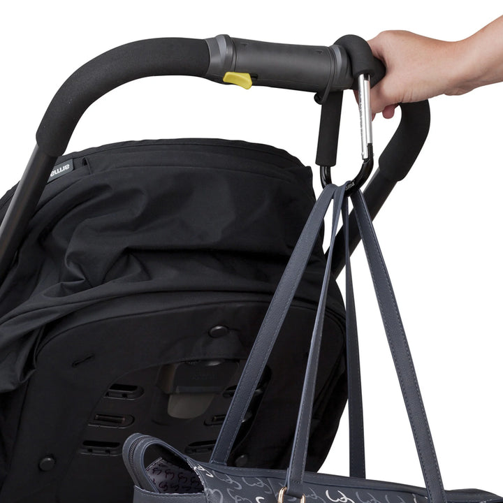 ClevaMama ClevaHooks stroller clips attached to a stroller handle, holding a bag while a hand grips the handle.