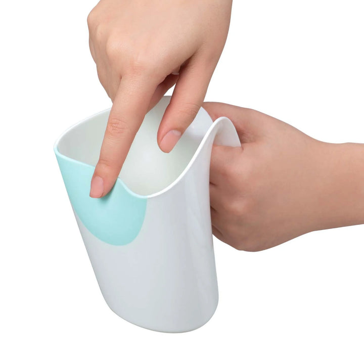 Hand demonstrating the soft, flexible rim of the ClevaMama ClevaRinse shampoo rinse cup with light blue insert, on a white background.