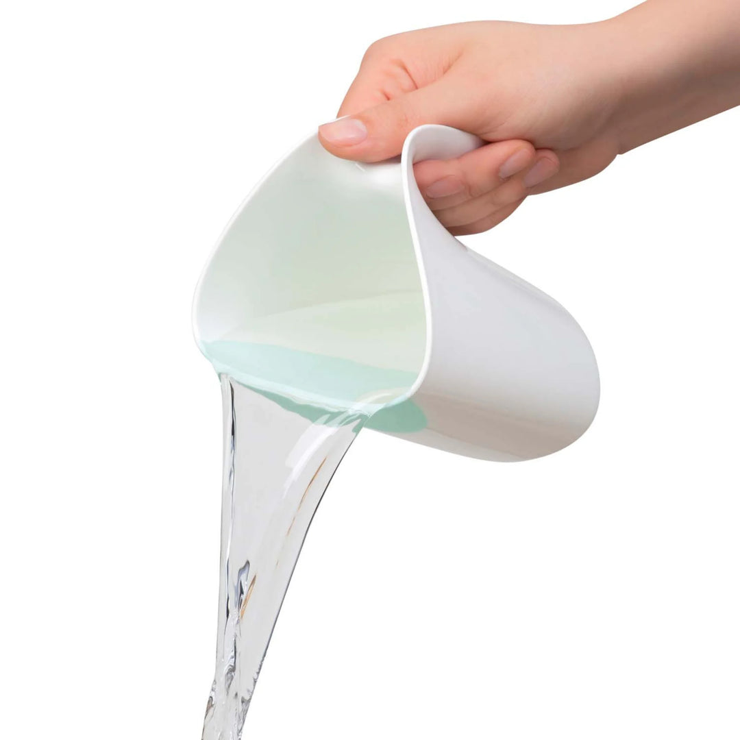 Hand pouring water from a ClevaMama ClevaRinse shampoo rinse cup, showing the flexible rim and controlled flow on a white background.