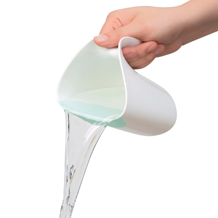 Hand pouring water from a ClevaMama ClevaRinse shampoo rinse cup, showing the flexible rim and controlled flow on a white background.