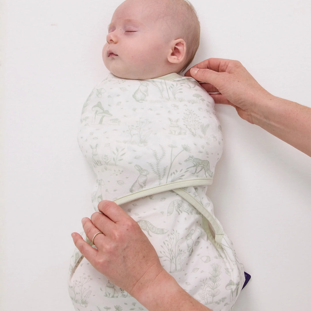 Parent adjusting ClevaMama ClevaSleep Forest Friends swaddle sleeping bag on sleeping newborn, baby sleep sack