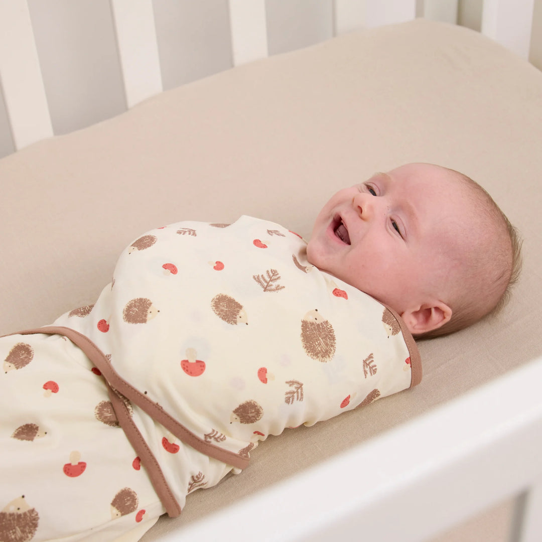 Baby in cot wearing ClevaMama ClevaSleep swaddle sleeping bag in hedgehog woodland print, newborn sleep sack