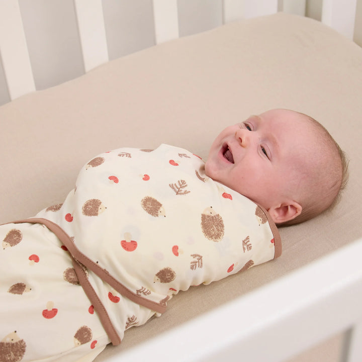 Baby in cot wearing ClevaMama ClevaSleep swaddle sleeping bag in hedgehog woodland print, newborn sleep sack