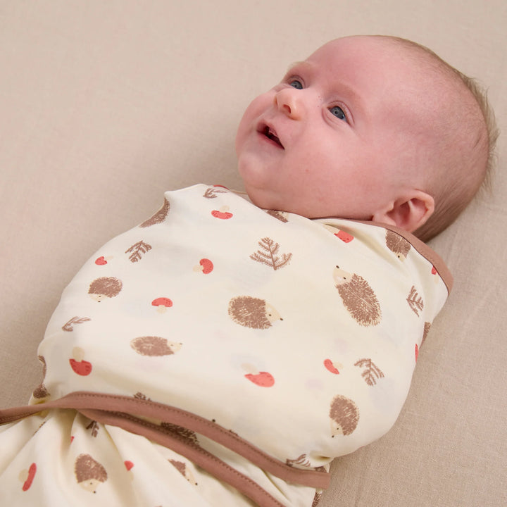 Baby lying on side in ClevaMama ClevaSleep swaddle sleeping bag, cream hedgehog woodland print newborn sleep sack
